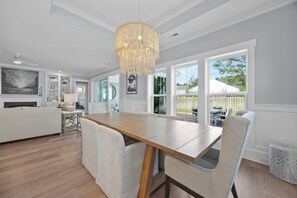 Une cuisine moderne avec une table en bois, des chaises blanches, un lustre et de grandes fenĂȘtres.