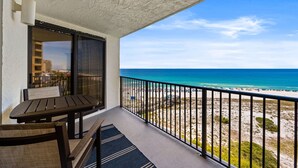 Un balcón con vista a la playa, una mesa y sillas.