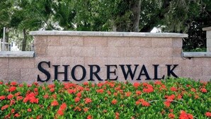 A stone wall with the word 'SHOREWALK' in large letters, surrounded by red flowers and greenery. - Shorewalk 2BR/2BA Condo Minutes from Beach & IMG (Bradenton)