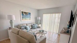 A living room with a beige sofa, two side tables with lamps, a framed picture on the wall, and a window with blinds. - Shorewalk 2BR/2BA Condo Minutes from Beach & IMG (Bradenton)