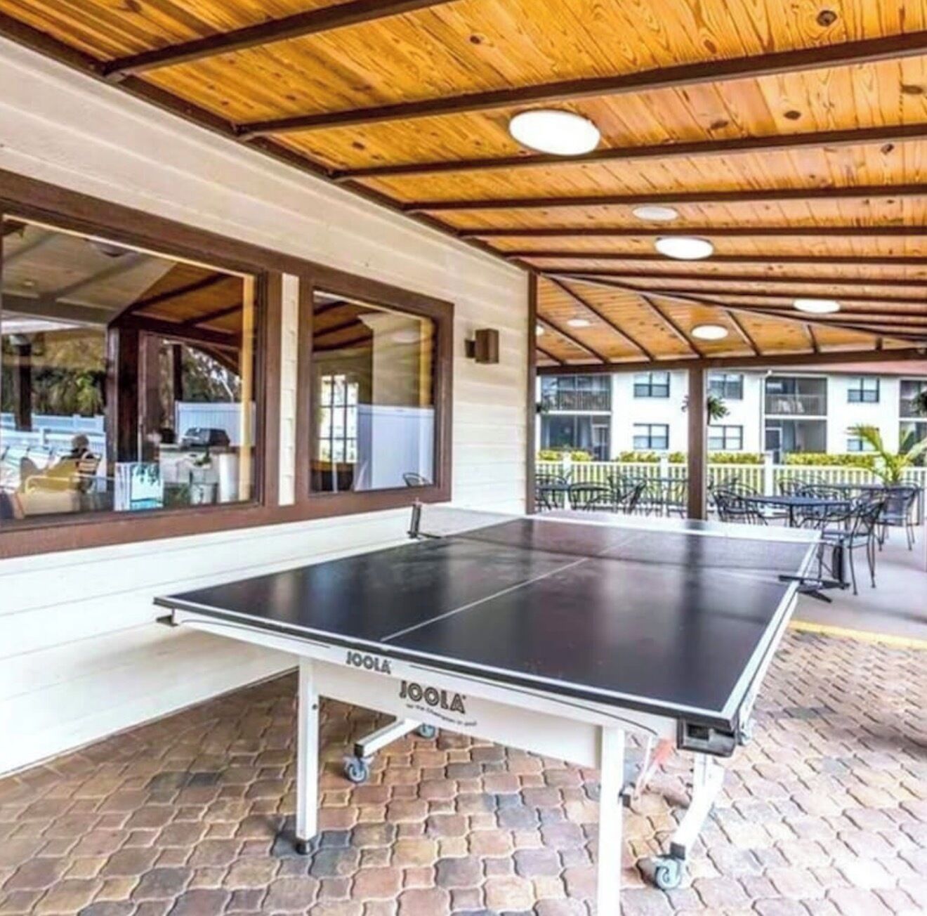 Une table de ping-pong extérieure dotée d’un plafond en bois et d’un sol en briques.
