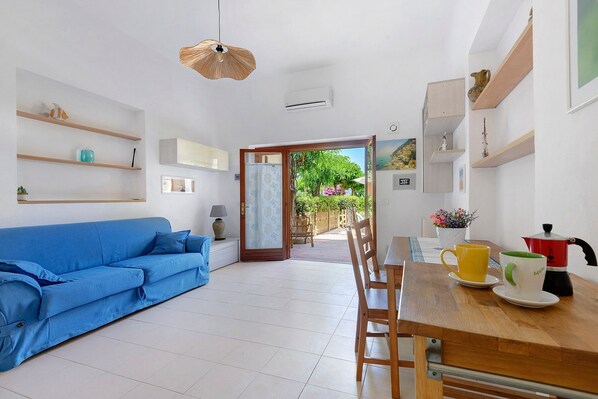A modern living room with a blue sofa, wooden dining table, and shelves with decorative items. - Apartment 'Stella Di Mare Beach' with Sea View, Private Terrace and Air Conditioning (Naregno)