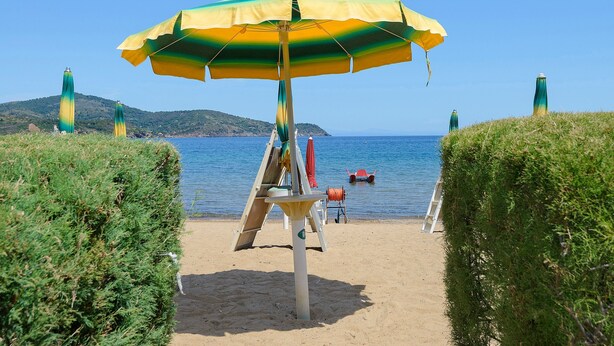 Ein Strand mit einem großen Sonnenschirm, einem Rettungsschwimmerstand und einem Boot im Wasser.