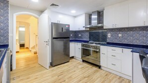 Et køkken med hvide skabe, et rustfrit stål køleskab, en komfur og en blålig backsplash med mønster.