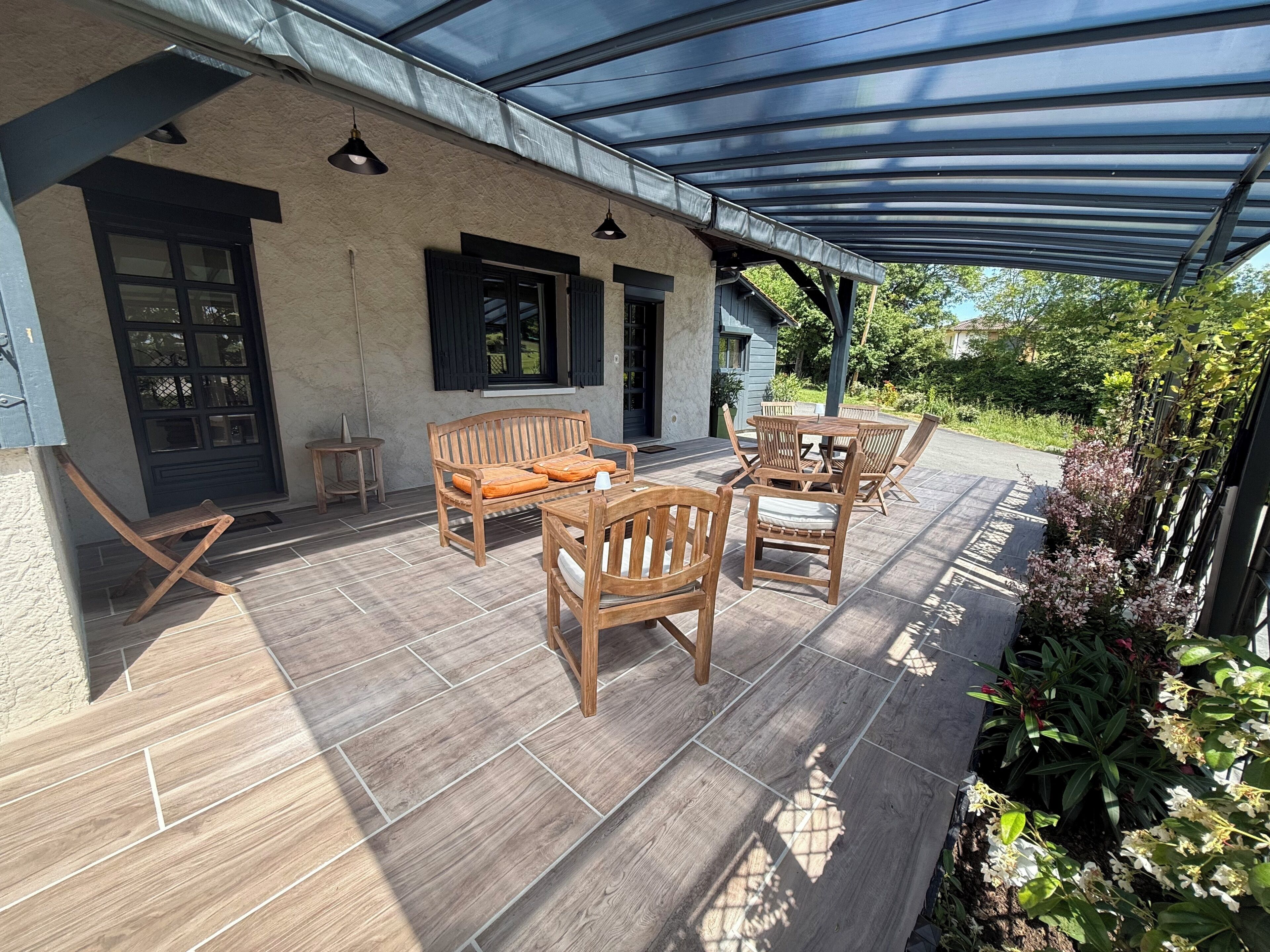 A covered patio with wooden furniture, a door, and a window.