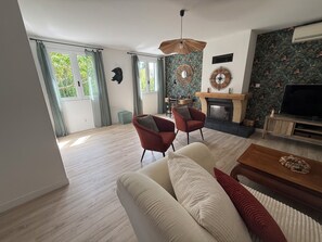 Een moderne woonkamer met een open haard, twee rode fauteuils, een bank en een televisie.
