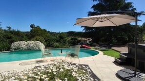 A swimming pool with clear blue water, surrounded by clear glass chairs and a large umbrella.