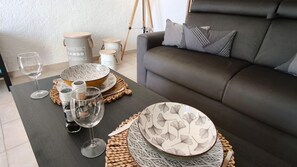 Une table à manger dressée avec des assiettes, des verres et un verre à vin, un canapé et, au fond, des boßtes de rangement.