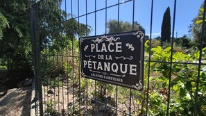 Une pancarte portant lâinscription « PLACE DE LA PĂTANQUE » est fixĂ©e derriĂšre une clĂŽture en mĂ©tal.