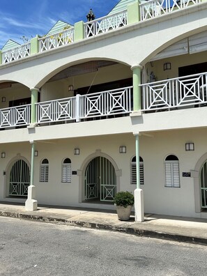 Ein mehrgeschossiges Gebäude mit weißer Fassade, grünen Akzenten und einem Balkon mit geometrischer Geländerkonstruktion.
