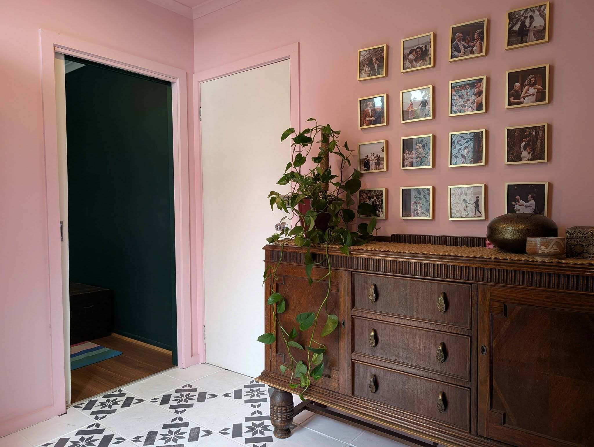 A hallway with a wooden dresser, a potted plant, and a wall of framed photographs.