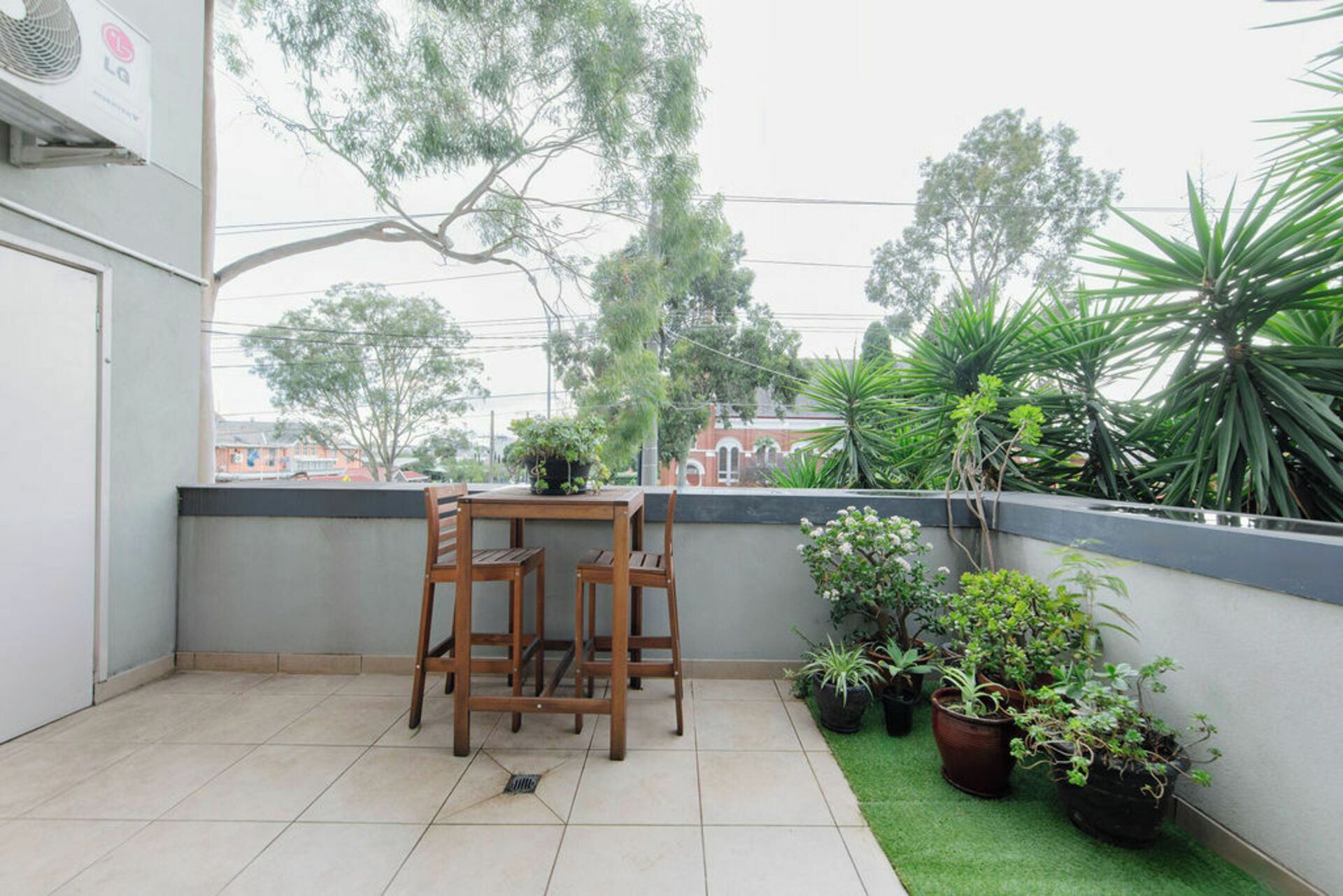 A balcony with a table and chairs, surrounded by potted plants and a view of the city.