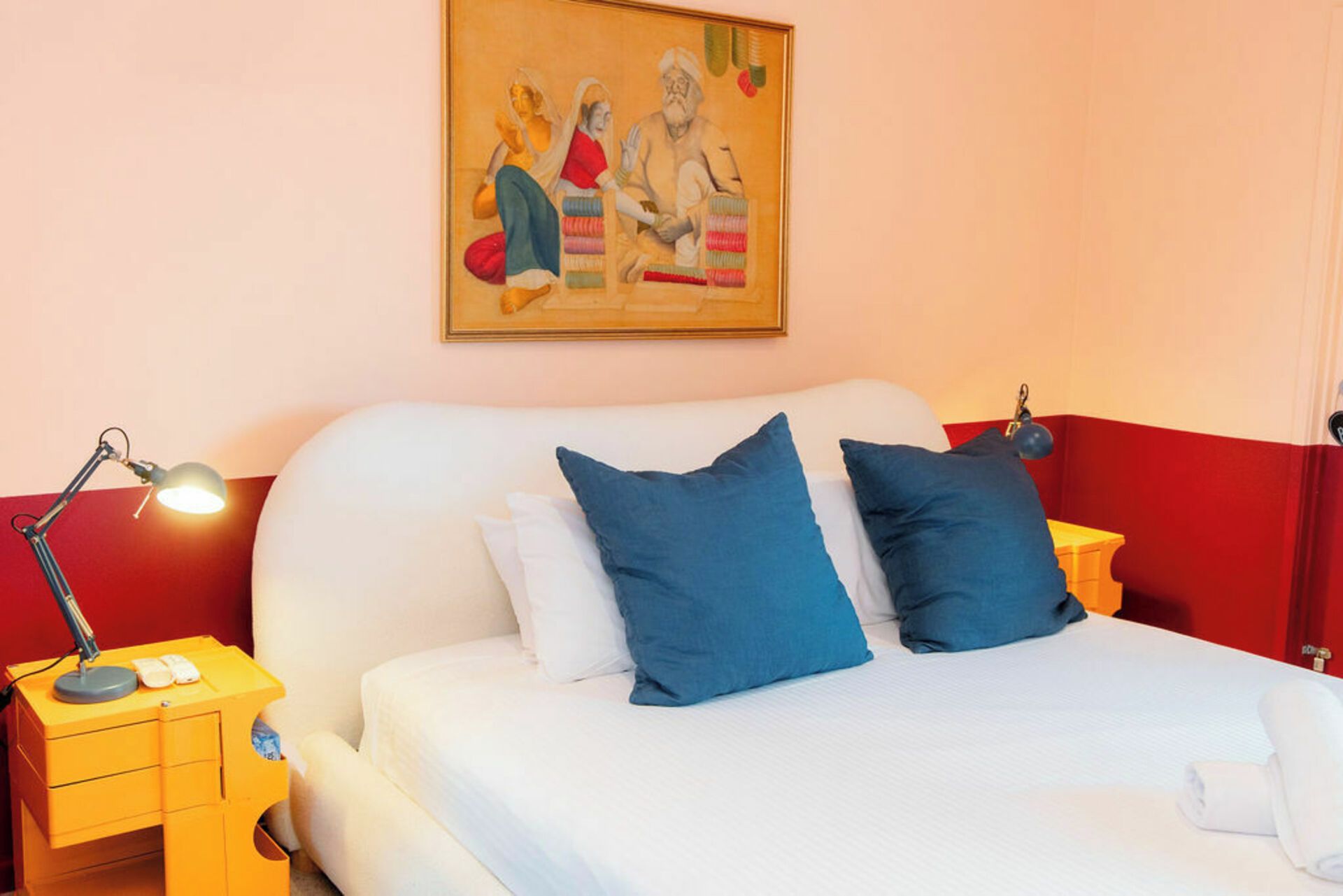 Une chambre d’hôtel avec un lit, des oreillers, un bureau avec une lampe et un tableau au mur.