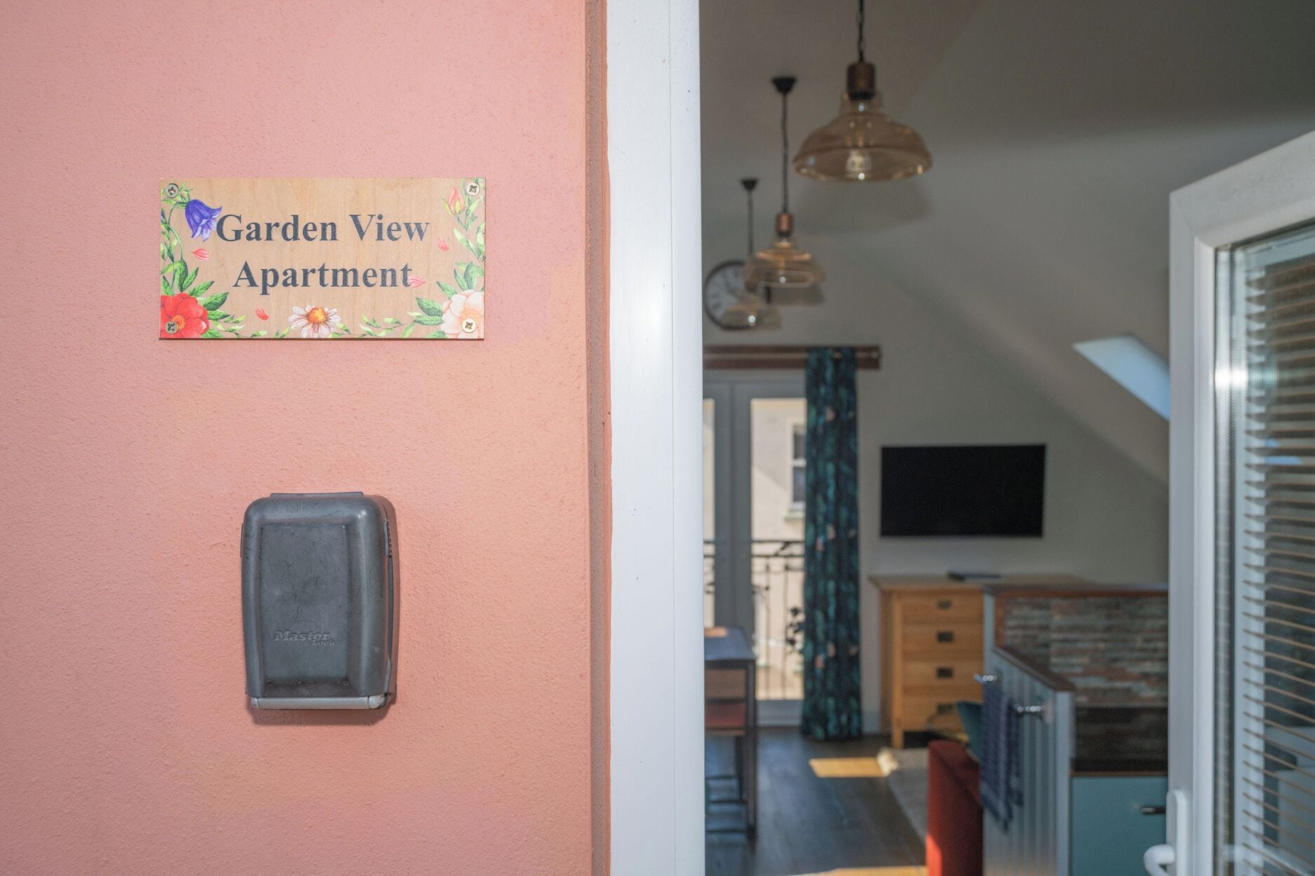 A hallway with a sign reading 'Garden View Apartment,' a doorbell, and a view into a room with a TV and a window.
