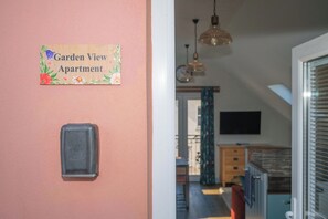 A hallway with a sign reading 'Garden View Apartment,' a doorbell, and a view into a room with a TV and a window. - Garden View Apartment (Kingsbridge)
