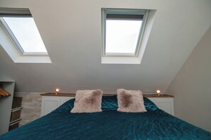 A bedroom with a skylight, a bed with a teal bedspread, and two fluffy pillows. - Garden View Apartment (Kingsbridge)