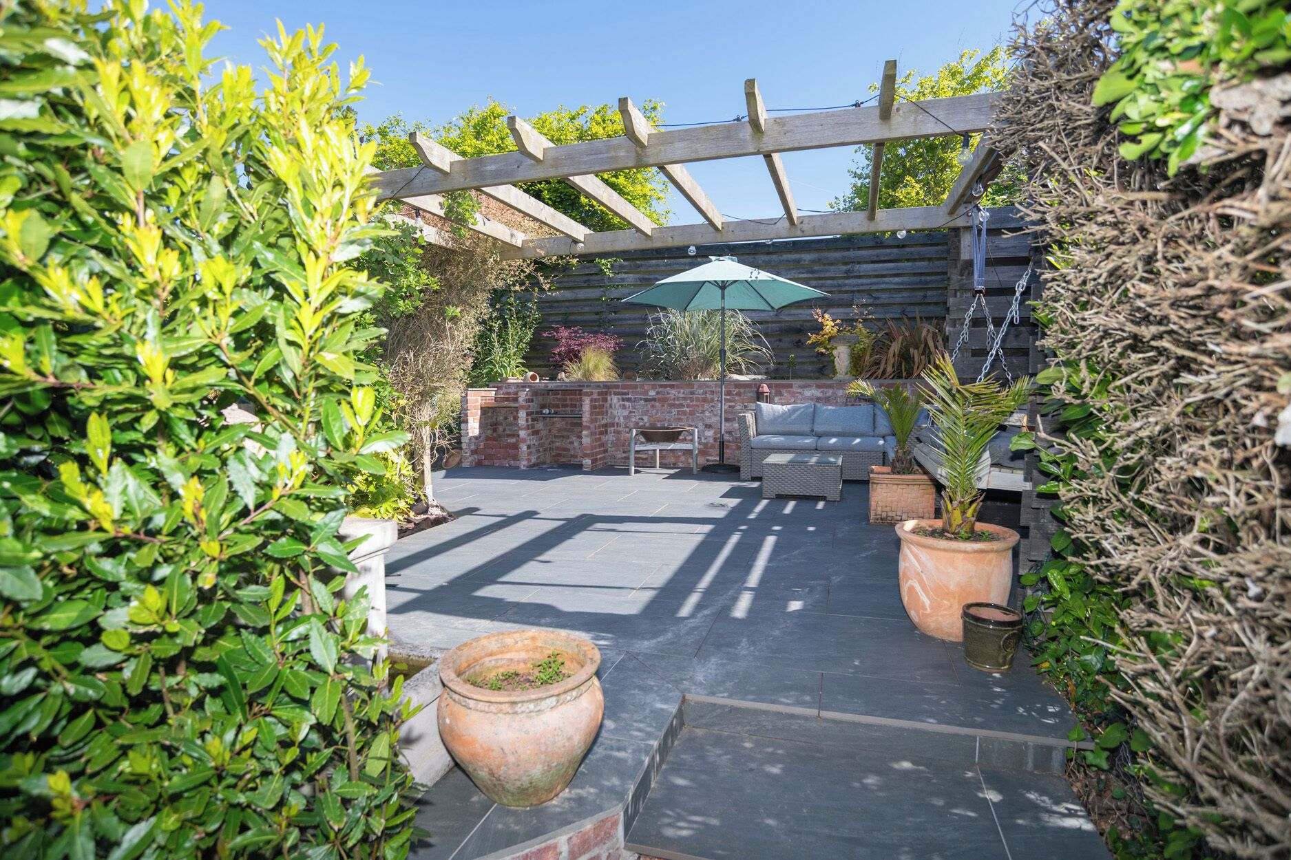 Un patio con un pérgola, mobiliario exterior y plantas en macetas.