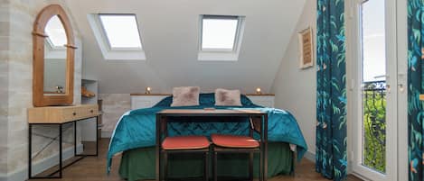 A bedroom with a skylight, a bed with pillows, a table with chairs, and a window with curtains.