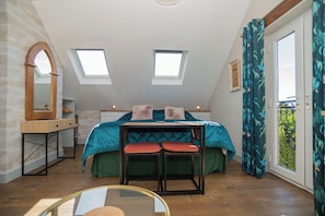 Et soveværelse med ovenlys, en seng med puder, et bord med stole og et vindue med gardiner.