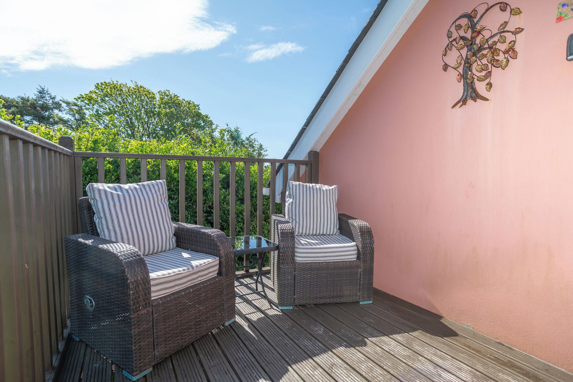 A balcony with wicker furniture, a glass table, and a decorative tree mural.