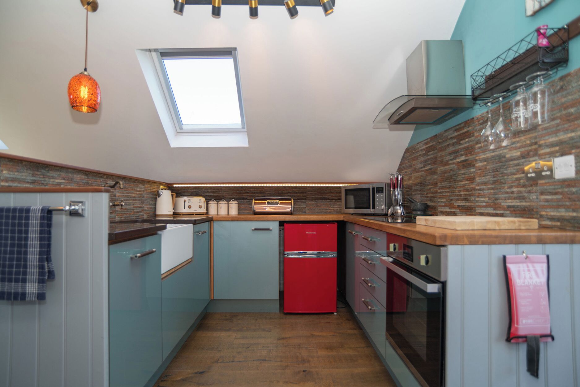 A compact kitchen with a skylight, a red dishwasher, and a microwave.