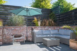 Eine Terrasse mit einem Korbsessel, einem runden Tisch und einem grünen Sonnenschirm.