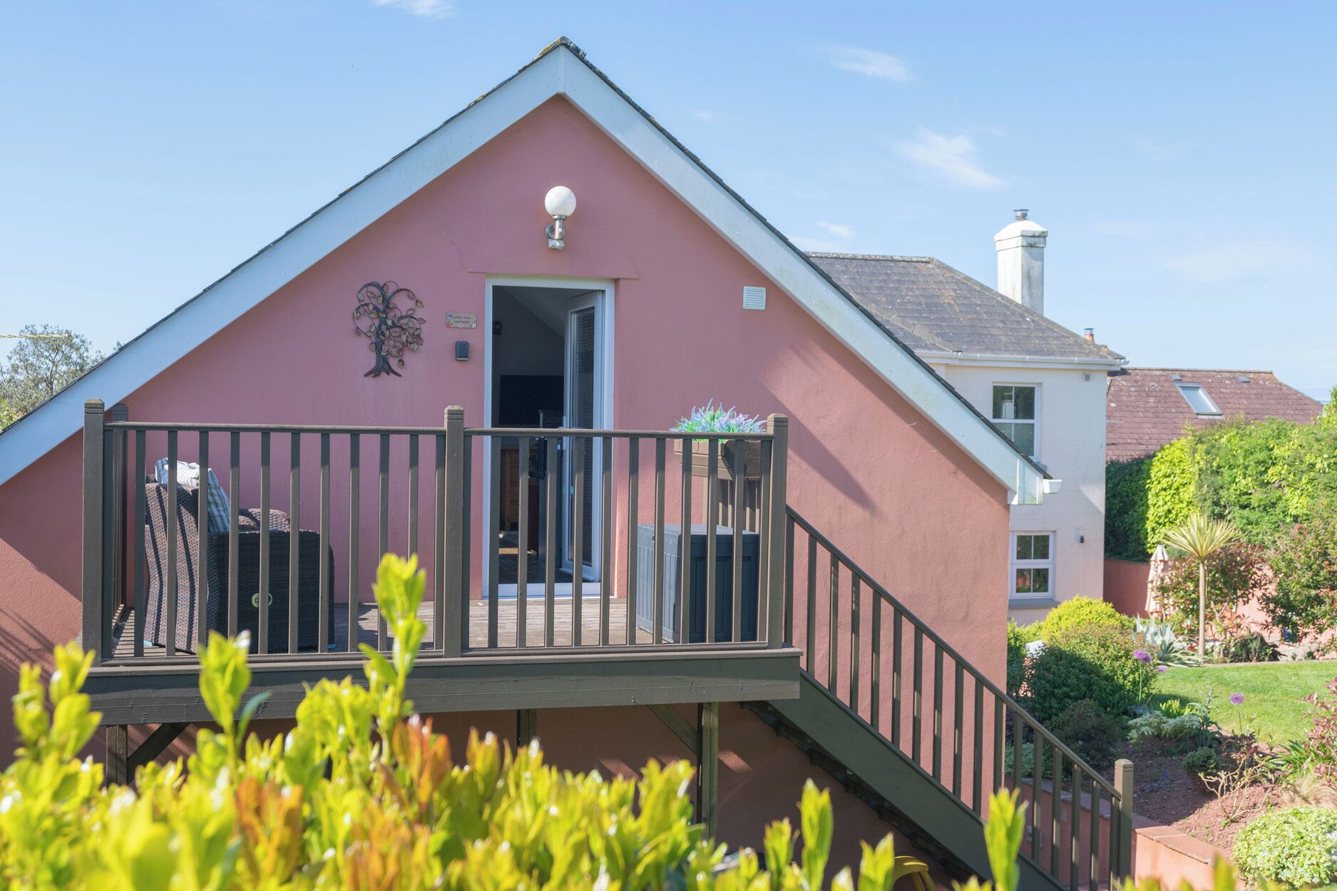 A pink building with a balcony, a door, and a small garden area.