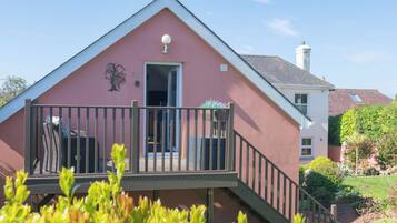 A pink building with a balcony, a door, and a small garden area.