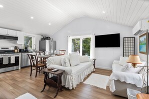 Eine moderne Küche mit weißen Schränken, ein Essbereich mit einem weißen Sofa und einem an der Wand montierten Fernseher.