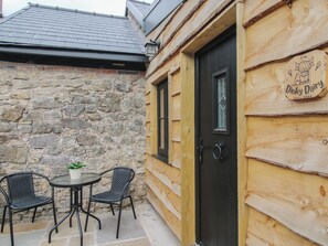 A wooden building with a stone wall, a black door, and a sign that reads 'Dinky Dairy.' There is a small table with two chairs outside. - The Dinky Dairy (Oswestry)