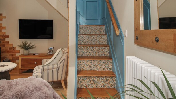 A staircase with a blue handrail, a wooden floor, a white radiator, and a flat-screen TV mounted on the wall. - The Dinky Dairy (Oswestry)