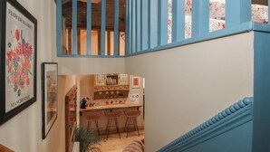 A staircase with blue railings leading to a kitchen area with bar stools and a potted plant. - The Dinky Dairy (Oswestry)