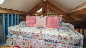 A loft bedroom with a sloped ceiling, wooden beams, a bed with floral bedding, and a skylight. - The Dinky Dairy (Oswestry)