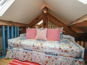 A loft bedroom with a sloped ceiling, wooden beams, a bed with floral bedding, and a skylight. - The Dinky Dairy (Oswestry)