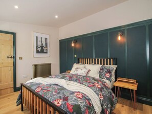 A bedroom with a wooden bed, a radiator, a framed picture on the wall, and a window with a view. - The Dinky Dairy (Oswestry)