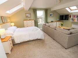 Un dormitorio con cama, sofá, cómoda, televisor y ventana con cortinas.