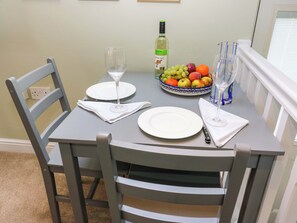 A dining table set with plates, a bowl of fruit, wine glasses, and a bottle of wine. - Chapel House Annex (Holmfirth)