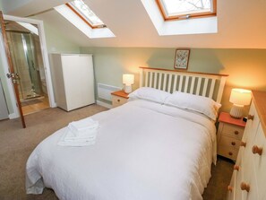 A bedroom with a bed, two bedside tables with lamps, a radiator, a wardrobe, and a shower area. - Chapel House Annex (Holmfirth)