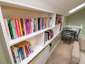 A bookshelf with various books, a dining table with chairs, and a radiator. - Chapel House Annex (Holmfirth)