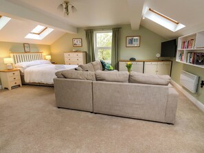 A bedroom with a bed, a sofa, a bedside table, a dresser, a radiator, a TV, and a bookshelf. - Chapel House Annex (Holmfirth)