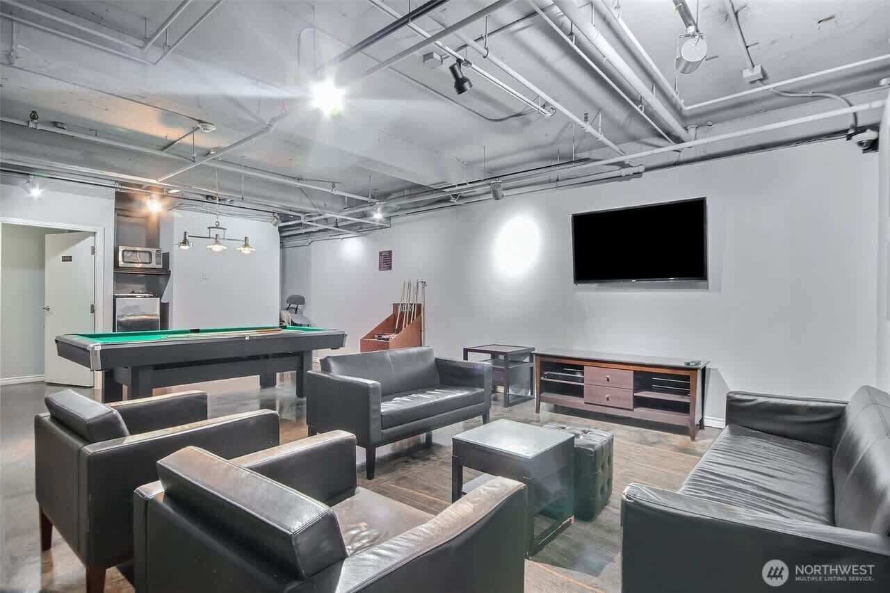 A modern lounge area with a pool table, leather sofas, a flat-screen TV, and a kitchenette.