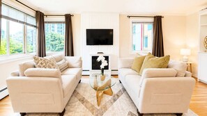 Ein modernes Wohnzimmer mit zwei Sofas, einem Glastisch, einem Flachbildfernseher und einem Kamin.