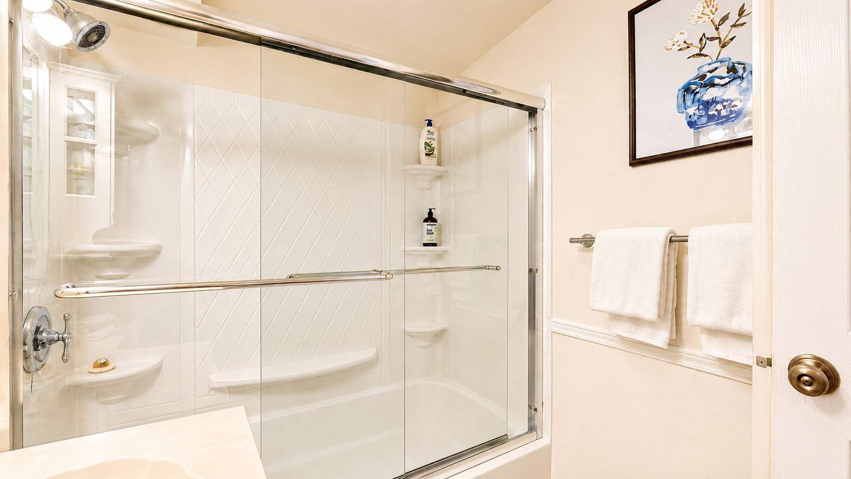 A modern bathroom with a glass shower enclosure, a white sink, and a framed artwork on the wall.