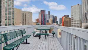 En tagterrasse med udsigt over byens skyline, med et bord og bænke.