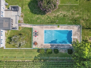 Vue aérienne d’une propriété résidentielle dotée d’une piscine, d’un patio avec des sièges et d’une cour clôturée.
