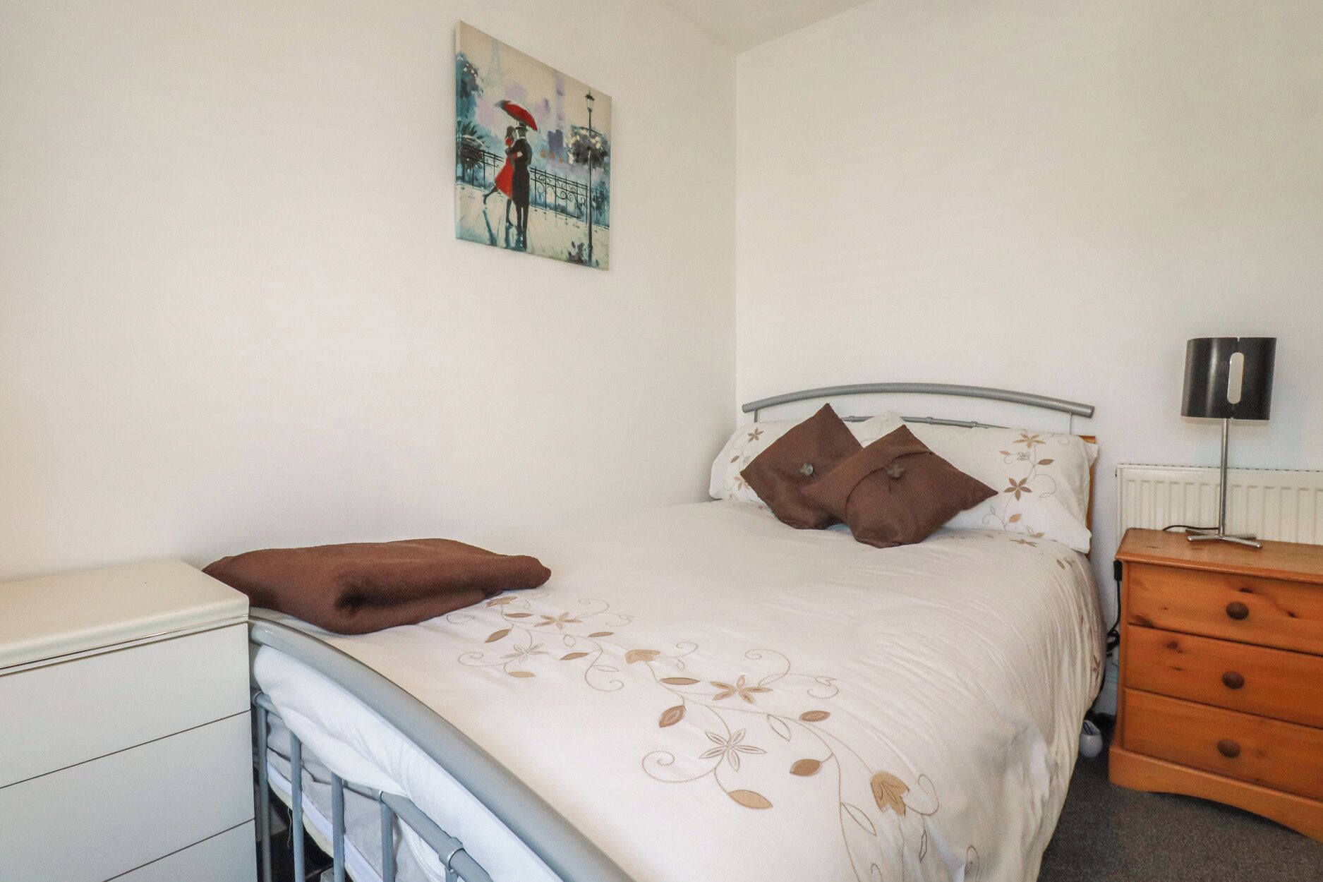A bedroom with a bed, a nightstand, a lamp, and a painting on the wall.
