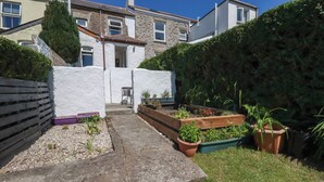 A residential property with a stone facade, a wooden deck, and raised garden beds. - Tin Lantern Cottage (Redruth)