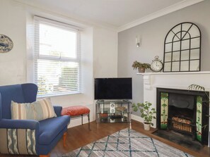 Un salón con un sofá azul, televisor de pantalla plana, chimenea y ventana con persianas.