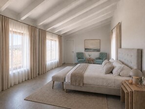 Ein Schlafzimmer mit einem großen Bett, zwei Sesseln, einem kleinen Tisch und einem Bild an der Wand.