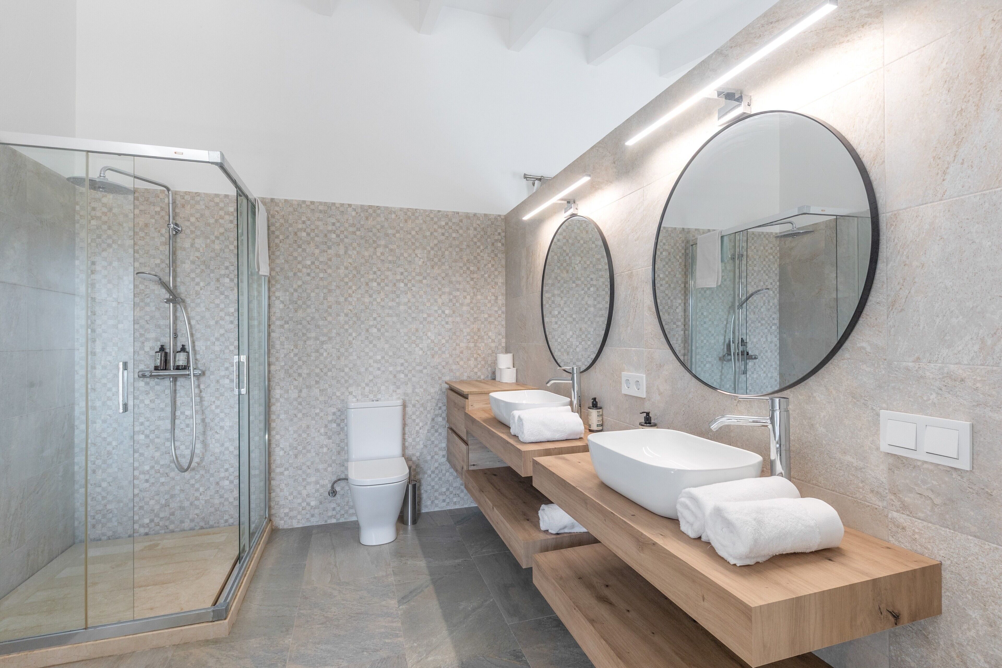 A modern bathroom with a glass shower enclosure, a toilet, and a vanity with two sinks and mirrors.